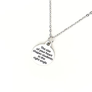 May include: Silver necklace with a round pendant that reads "The size of your heart shapes students in the right angle".