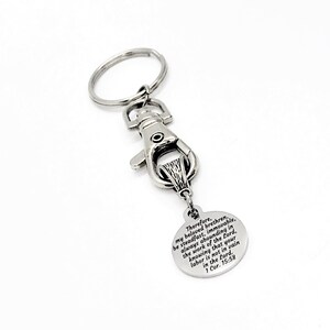 May include: Silver keychain with a round charm featuring the Bible verse "Therefore, my beloved brethren, be steadfast, immovable, always abounding in the work of the Lord, knowing that your labor is not in vain in the Lord. 1 Cor. 15:58."