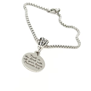 May include: Silver-toned bracelet with a round charm. The charm is engraved with the words "Trust in the Lord with all your heart. Proverbs 3:5." The bracelet has a decorative bead and a chain-link design.