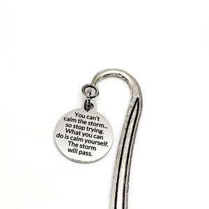 Puede incluir: Marcapáginas de plata con un encanto redondo que dice "You can't calm the storm... so stop trying. What you can do is calm yourself. The storm will pass."
