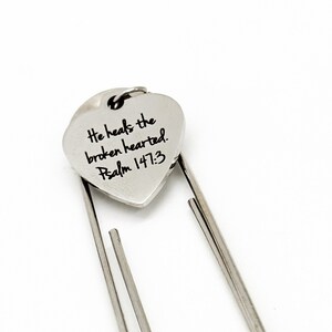 May include: Silver heart-shaped bookmark with the text "He heals the broken hearted. Psalm 147:3" engraved on it.