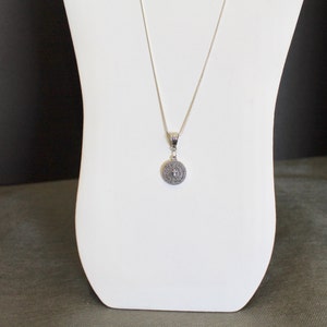 May include: A silver chain necklace with a round pendant featuring a cross and the words "Believe in the impossible".