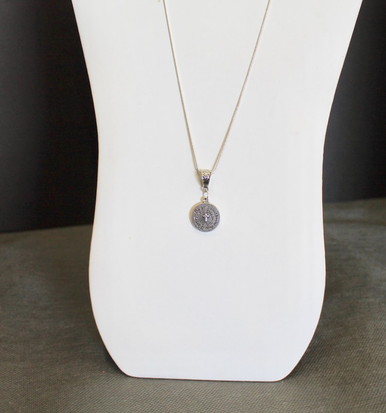 May include: A silver chain necklace with a round pendant featuring a cross and the words "Believe in the impossible".