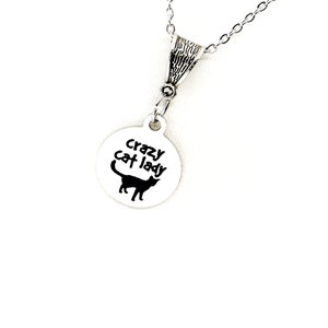 Puede incluir: Collar de plata con un colgante redondo que dice "crazy cat lady" con una silueta negra de un gato.