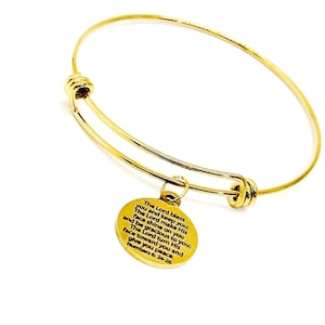 May include: Gold bangle bracelet with a round charm that has a bible verse from Numbers 6:24-26 inscribed on it. The verse reads: "The Lord bless you and keep you; The Lord make His face shine on you and be gracious to you; The Lord turn His face toward you and give you peace."
