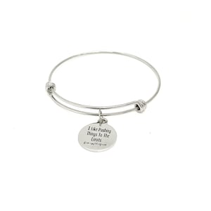 May include: Silver bangle bracelet with a charm that reads "I like pushing things to the limits".