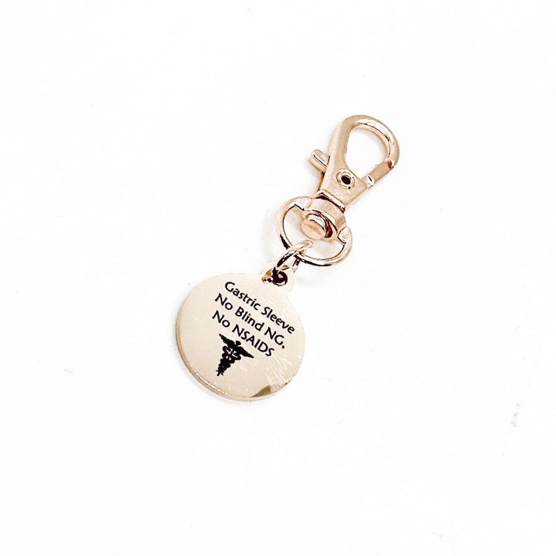 May include: Gold-toned keychain with a round tag that reads "Gastric Sleeve No Blind NG. No NSAIDS" with a medical symbol.