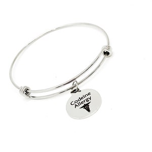 May include: Silver bangle bracelet with a round charm that says "Codeine Allergy" with a medical symbol.
