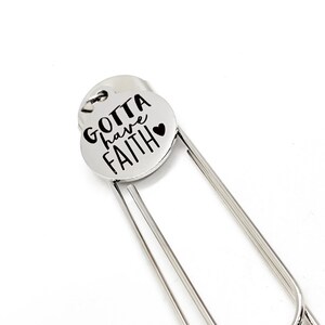 May include: Silver bookmark with a round charm that says "Gotta have faith" with a small heart.