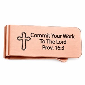 May include: A copper-coloured money clip featuring a cross and the inscription "Commit Your Work To The Lord Prov. 16:3". The clip is designed to hold money and cards, with a curved edge.