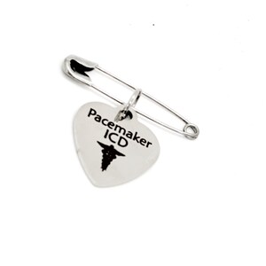 May include: Silver heart-shaped medical alert pin with a safety pin attachment. The heart has the text "Pacemaker ICD" and a medical symbol.