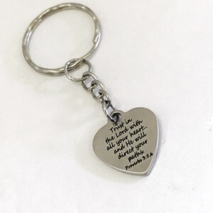 May include: Silver heart-shaped keychain with a silver chain and ring. The heart has the text "Trust in the Lord with all your heart... and He will direct your paths Proverbs 3:5,6" engraved on it.