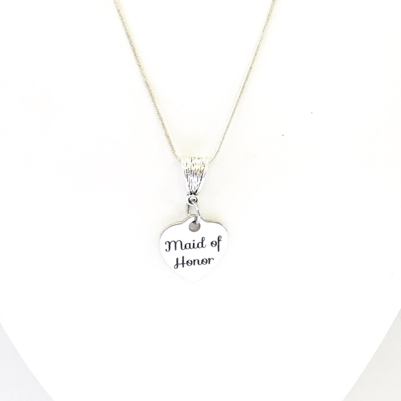 Puede incluir: Collar de plata con un colgante en forma de coraz&oacute;n que dice "Maid of Honor".