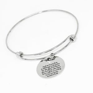 Può includere: Un braccialetto a cerchio color argento con un ciondolo circolare. Il ciondolo presenta un messaggio inciso da Romani 8:28. Il braccialetto è realizzato in un materiale metallico lucido ed è regolabile.