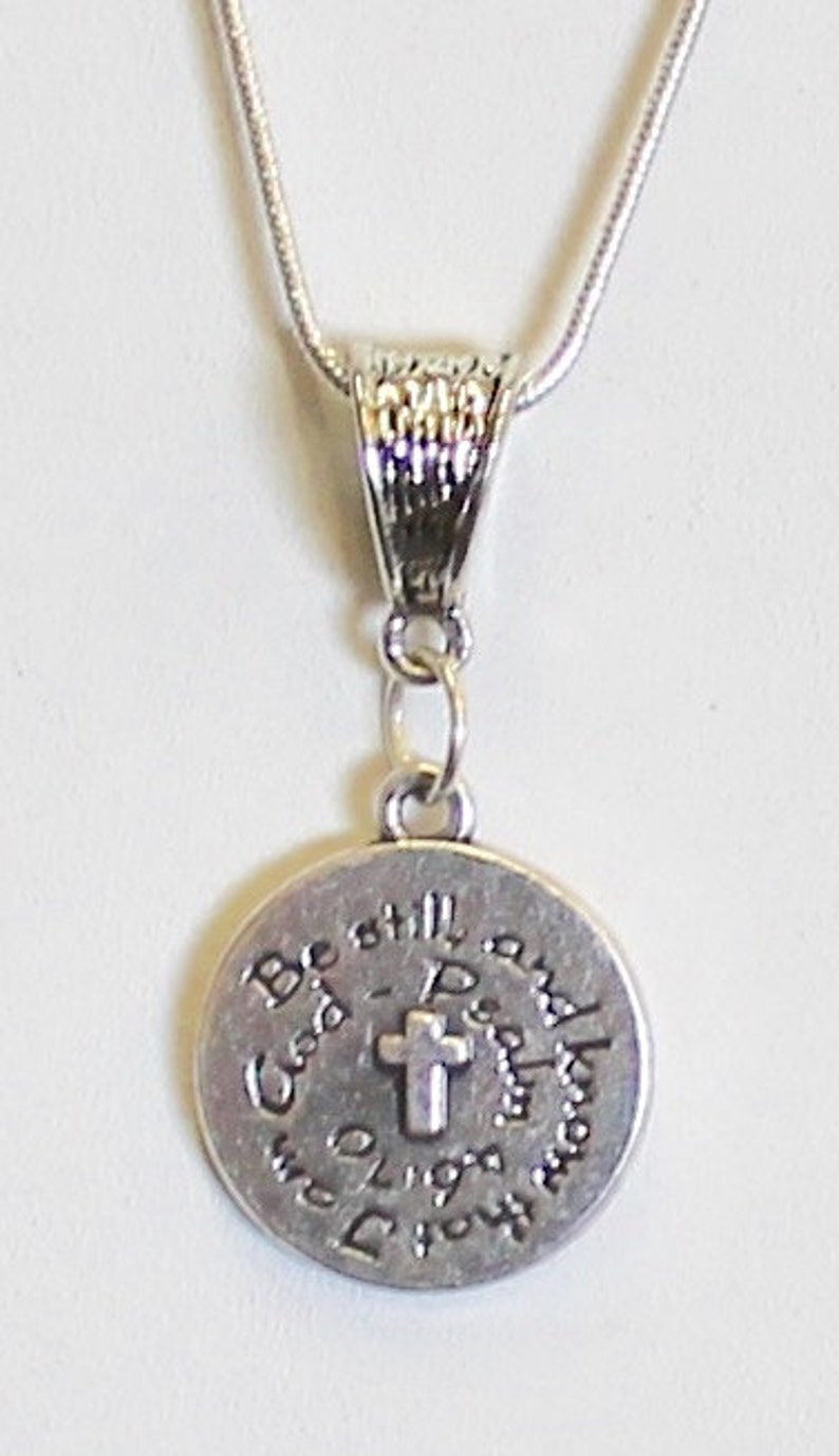 May include: Silver necklace with a round pendant that says "Be still and know that I am God" with a small cross in the center.
