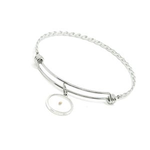 May include: Silver-toned bangle bracelet with a twisted rope design. The bracelet features a circular charm with a small, light-brown seed encased within. The charm hangs from a curved bar, adding a delicate touch to the jewelry.