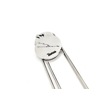 May include: Silver bookmark with a circular charm featuring the Taurus constellation and the word "Taurus" engraved on it.