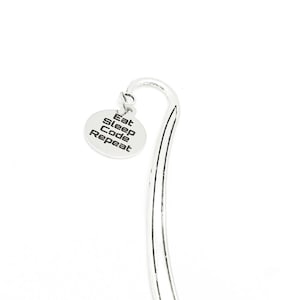 Może przedstawiać: Srebrna zakładka do książki z okrągłym wisiorkiem z napisem "Eat Sleep Code Repeat".