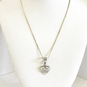 May include: A silver chain necklace with a heart-shaped pendant that reads "my heart belongs to a firefighter".