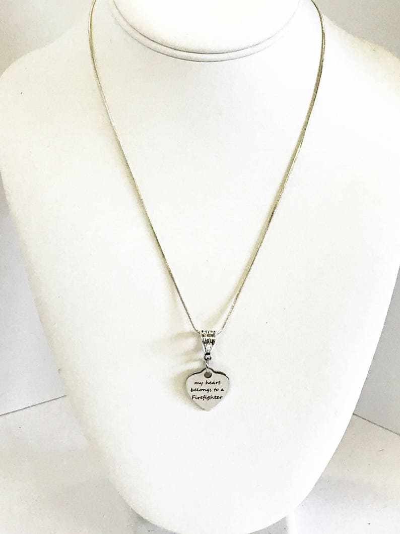 May include: A silver chain necklace with a heart-shaped pendant that reads "my heart belongs to a firefighter".
