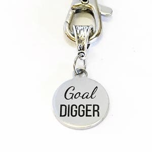 May include: Silver keychain with a round charm that says "Goal Digger" in black lettering.