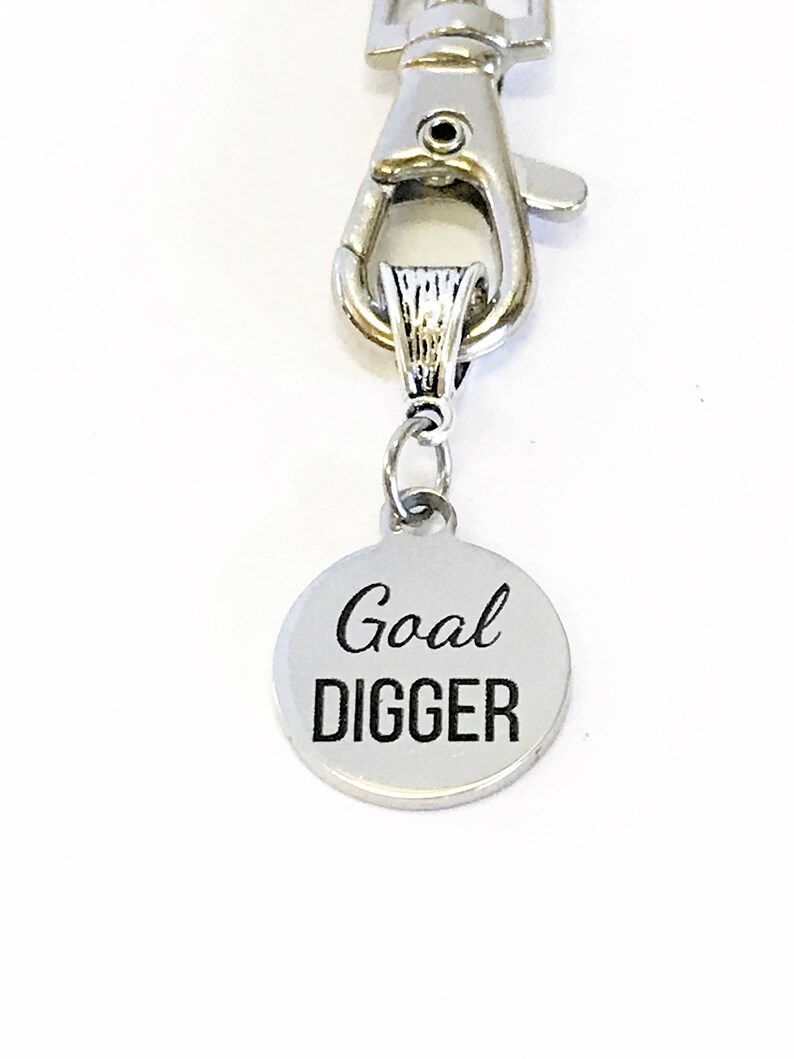 May include: Silver keychain with a round charm that says "Goal Digger" in black lettering.