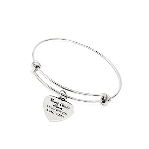 May include: Silver bangle bracelet with a heart charm that reads "Boy (boi) noun. A noise with dirt & grass stains."