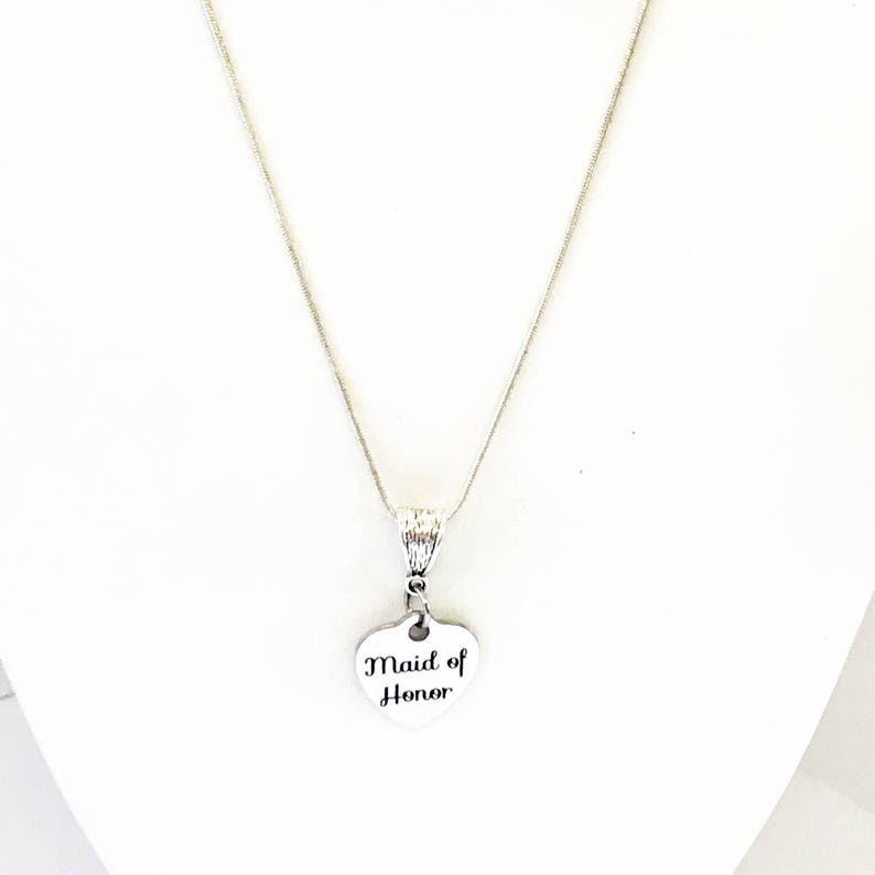 Puede incluir: Un collar de plata con un colgante en forma de coraz&oacute;n que dice "Maid of Honor".