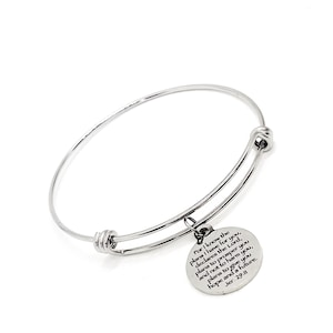 May include: A silver-colored adjustable bangle bracelet with a round charm. The charm has engraved text from Jeremiah 29:11. The bracelet is made of a shiny, metallic material and is displayed on a white background.