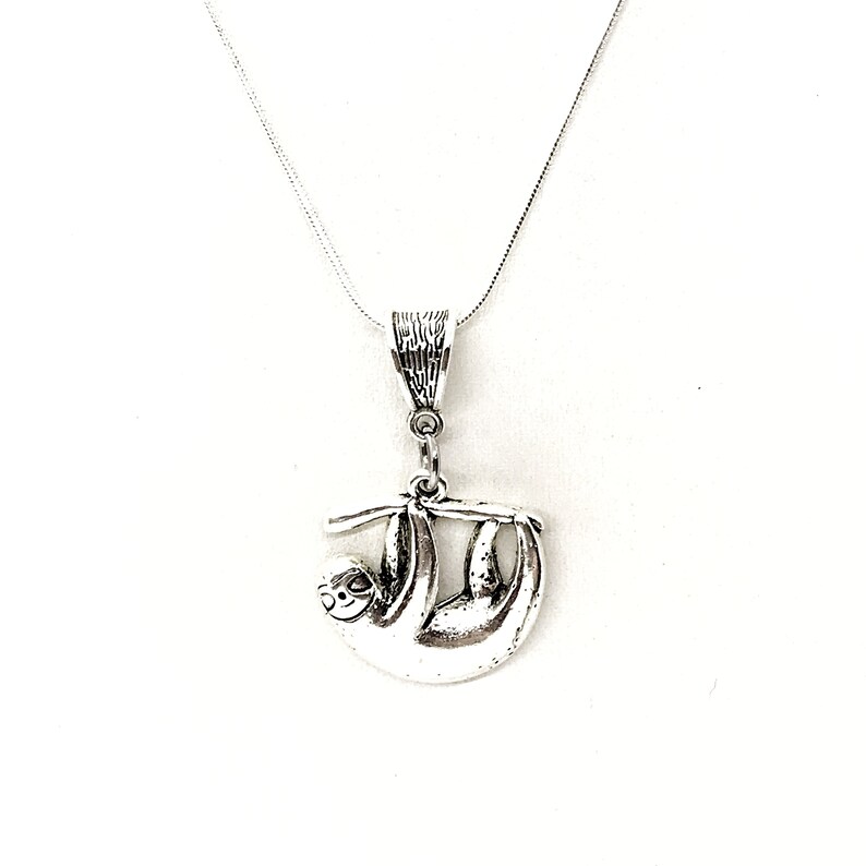 May include: A silver necklace with a pendant shaped like a sloth hanging from a branch. The pendant is detailed and has a textured finish.