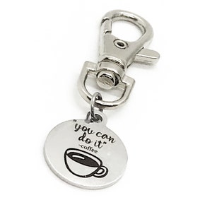 May include: Silver keyring with a round charm that says "you can do it" with a coffee cup icon and the text "coffee" underneath.