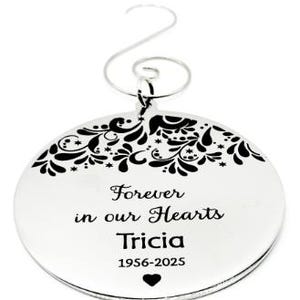 Può includere: Ornamento natalizio ovale color argento con bordo floreale. L'iscrizione "Forever in our Hearts Tricia 1956-2025" è incisa con un cuore. Ha un gancio argentato per appenderlo. Diametro di circa 8 cm.