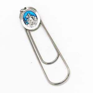 Puede incluir: Marcapáginas de plata con un encanto ovalado azul y plateado que representa a San Cristóbal. El encanto tiene el texto "Saint Christopher" alrededor del borde.