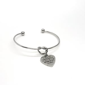 以下が含まれることがあります： 天使の羽根の音が聞こえる。あなたはまだ私たちと一緒です。というメッセージが刻まれたハート型のチャームが付いたシルバーのバングルブレスレットです。