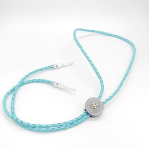 May include: A light blue bolo tie with a silver bullet tip and a braided leather cord.