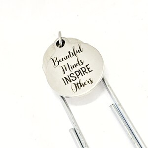 May include: Silver bookmark with a round charm that says "Beautiful Minds Inspire Others".