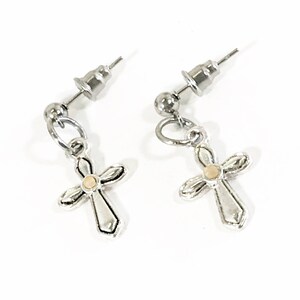 May include: A pair of silver stud earrings with a small cross charm. Each cross has a small gold center.