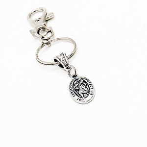 May include: Silver keychain with a silver oval charm featuring a depiction of Saint Christopher and the text "ST CHRISTOPHER PROTECT US".