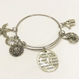 Może przedstawiać: Srebrna bransoletka z zawieszką w kształcie muszli, gwiazdą morską i zawieszką z tekstem "may you always have a shell in your pocket & sand between your toes".