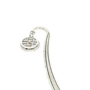 May include: A silver-toned bookmark with a curved top and a circular charm. The charm features text that reads "I have a mustard seed and I'm no afraid". The bookmark is designed for use in books.