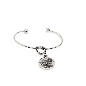 May include: A silver-colored open cuff bracelet with a knot design and a circular charm. The charm has engraved text from Isaiah 54:17. The bracelet features small ball accents at the open ends.