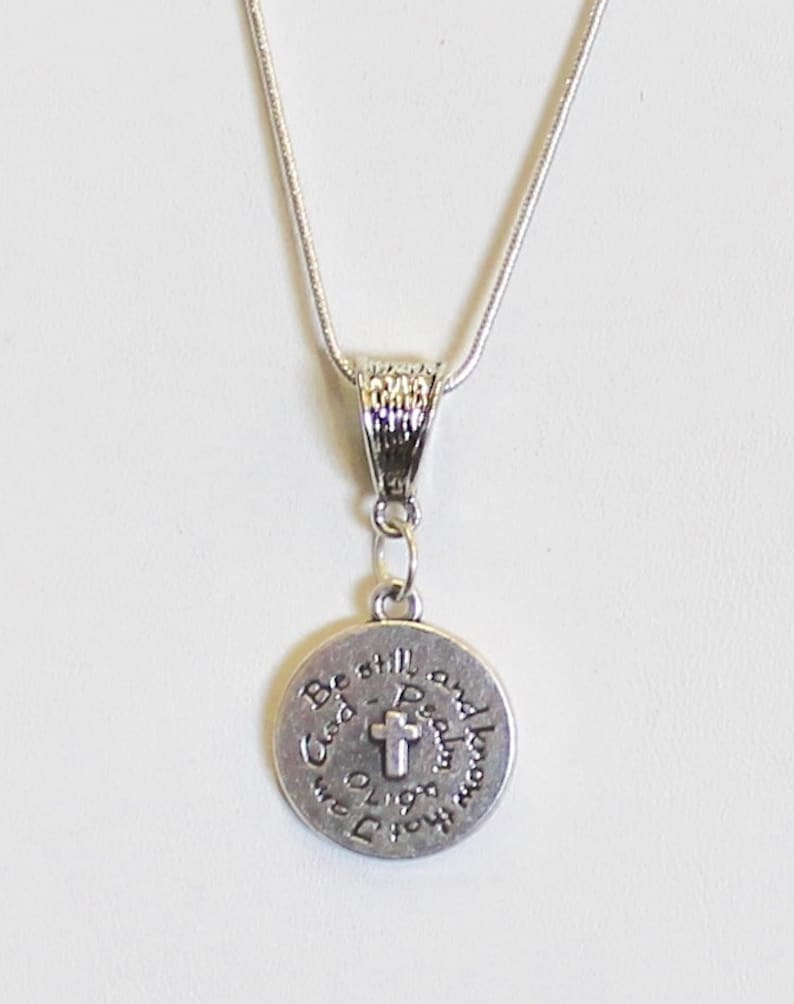 May include: A silver necklace with a round pendant that says "Be still and know that I am God" with a cross in the center.