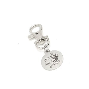 May include: Silver keychain with a round tag that says "Love one another" with a floral design.