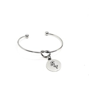 May include: Silver bangle bracelet with a knotted design and a charm featuring a delicate flower illustration.