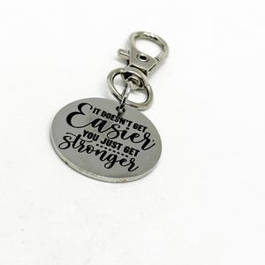 Puede incluir: Llavero de plata con una etiqueta redonda que dice "It doesn't get easier, you just get stronger".