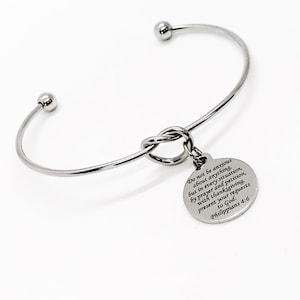 May include: A silver bangle bracelet with a knot charm. The charm has an inscription that reads: "Do not be anxious about anything, but in every situation, by prayer and petition, with thanksgiving, present your requests to God. Philippians 4:6"