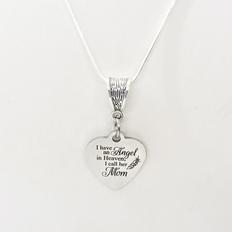 May include: Silver necklace with a heart-shaped pendant that reads "I have an Angel in Heaven, I call her Mom". The pendant has a small feather design.