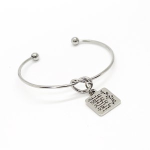 May include: Silver bangle bracelet with a knotted charm. The charm has a square tag with the inscription "Behind you, all your memories. Before you, all your dreams. Around you, all who love you. Within you, all you will ever need."