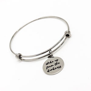 May include: Silver bangle bracelet with a charm that reads "Wake up from the darkness".