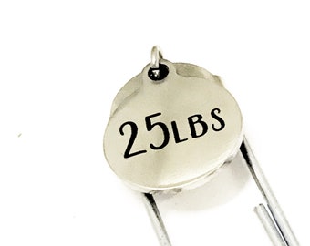 May include: Silver-toned metal bookmark with a round tag that says "25 LBS" in black lettering.